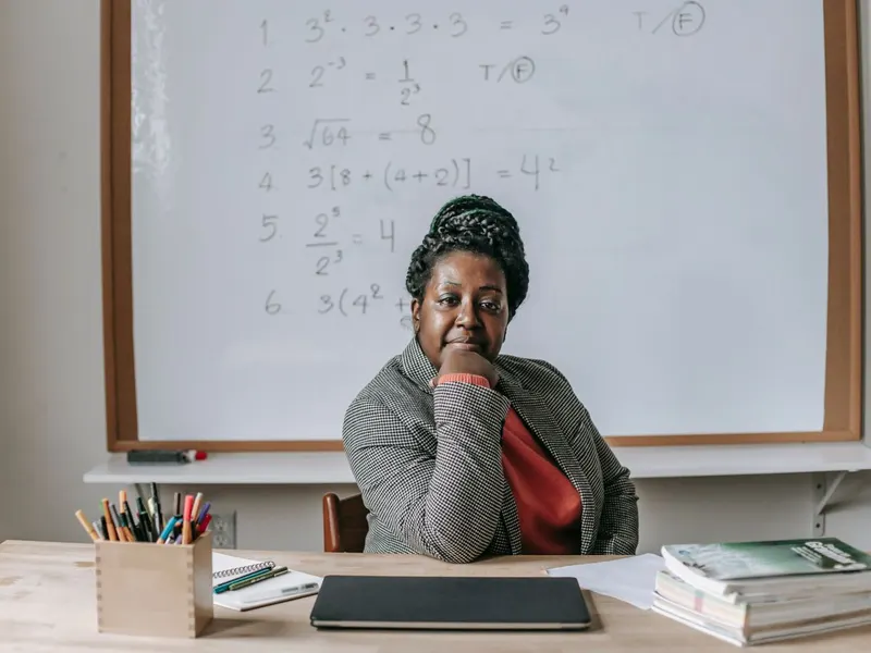 A school administrator seated at a desk with books, pens and a laptop in front of a whiteboard